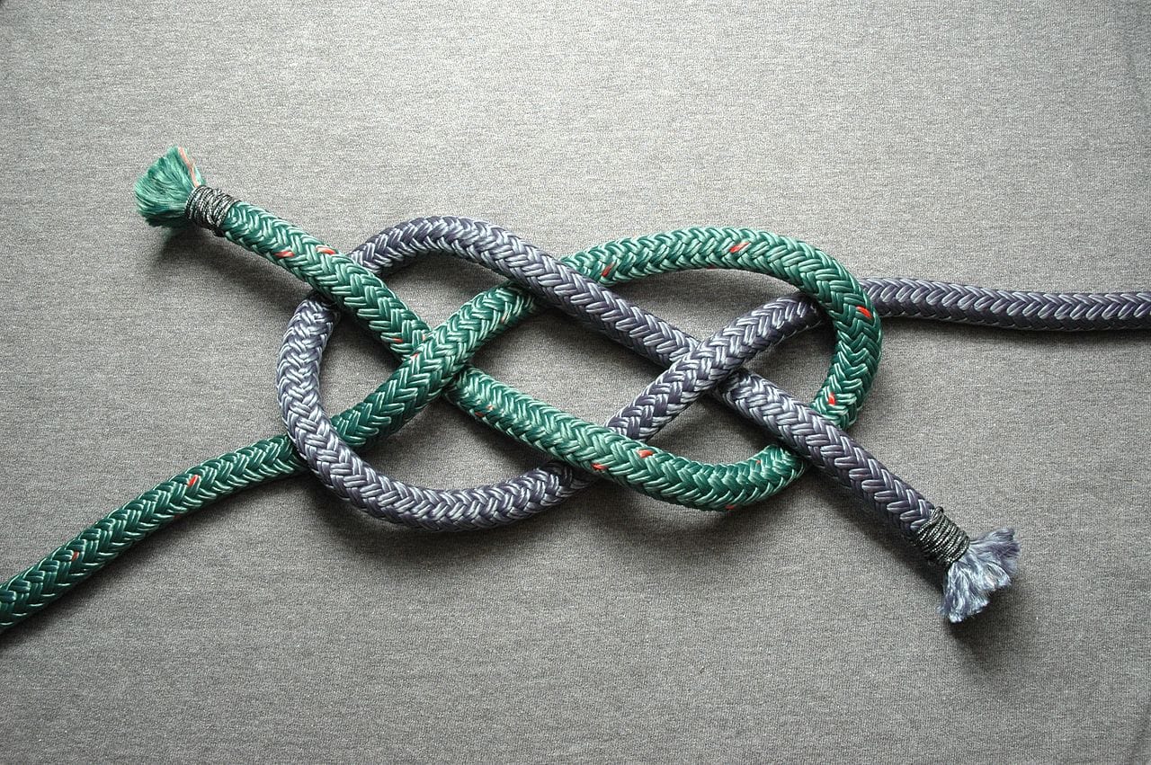 Loose Carrick knot joining a silver and a green rope together with a light gray background.